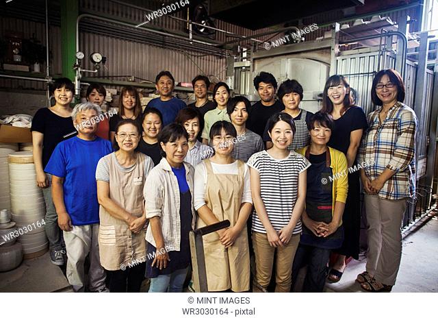 Group portrait of the staff of a Japanese porcelain workshop standing in front of kiln, smiling at camera