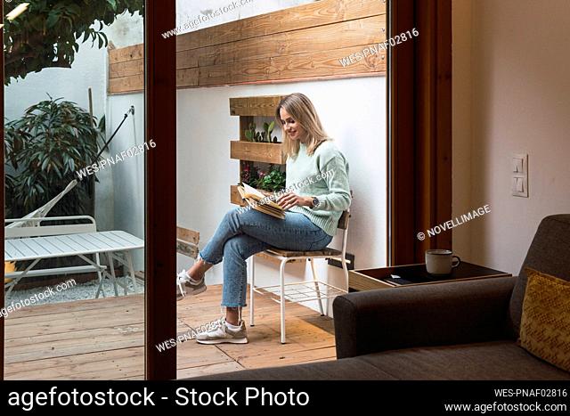 Woman reading book sitting on chair at patio