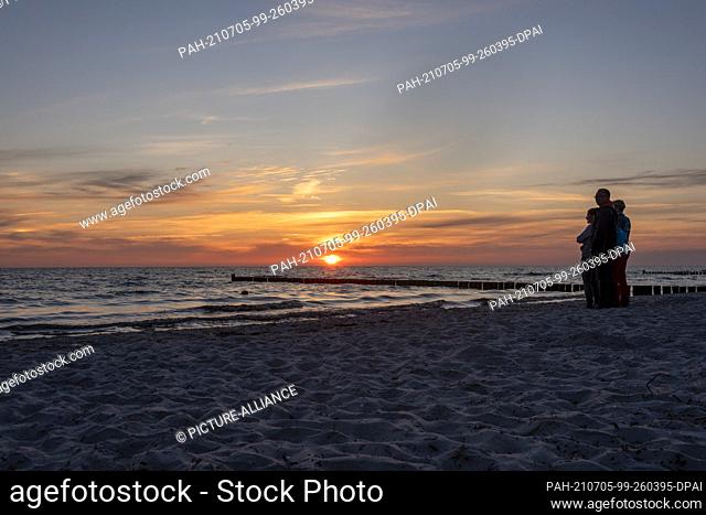 25 June 2021, Mecklenburg-Western Pomerania, Hiddensee: Holidaymakers stand on the beach of Vitte and enjoy a colourful sunset