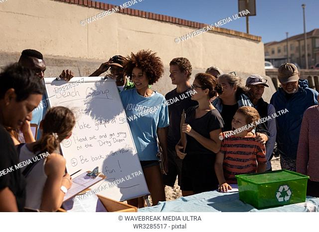 Front view of group of multi ethnic people looking at a board with volunteering rules at the beach