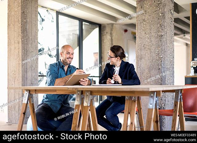 Smiling businessman writing in notepad while sitting by woman at office