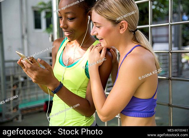 Smiling woman with hands on shoulder of friend using smart phone