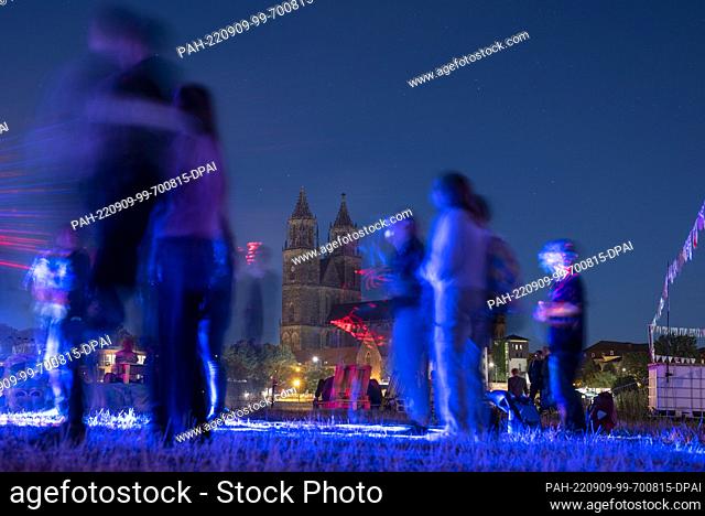 09 September 2022, Saxony-Anhalt, Magdeburg: Festival visitors dance on the Elbe meadows in front of Magdeburg Cathedral