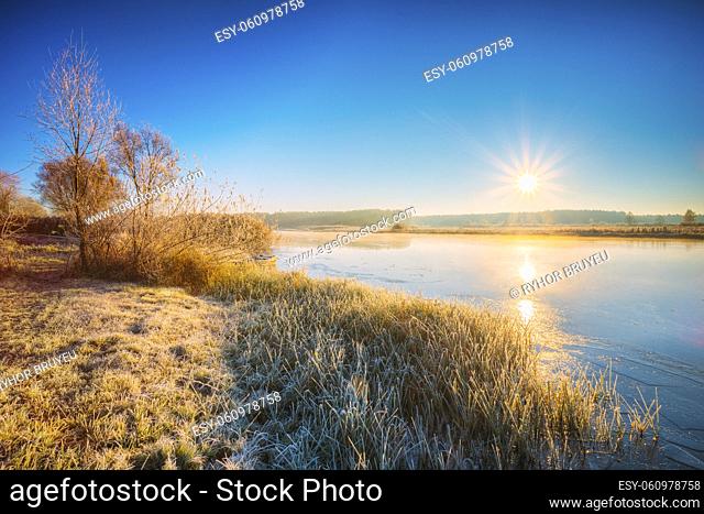 Sun Rises Over River. Autumn Frost Frozen River Covered With Thin Ice. Grass Covered With Frost. Sunrise, Sunset Over Autumn River