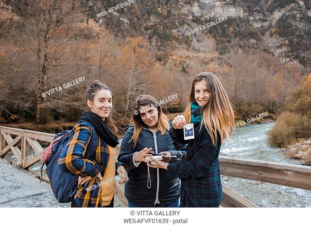 Spain, portrait of three young women with instant photos on a bridge in Ordesa National Park