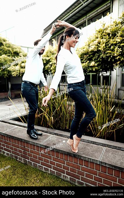 Carefree colleagues dancing on retaining wall outside industry