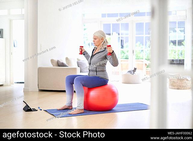 Senior woman exercising while learning from online tutorial through digital tablet at home
