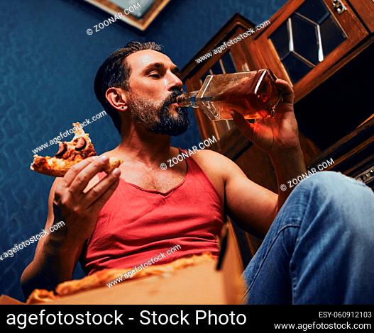 Bearded Man Lover of Alcoholic Beverages. He Eats Pizza in Home. The Man Looks Brutal. Close Up Shote