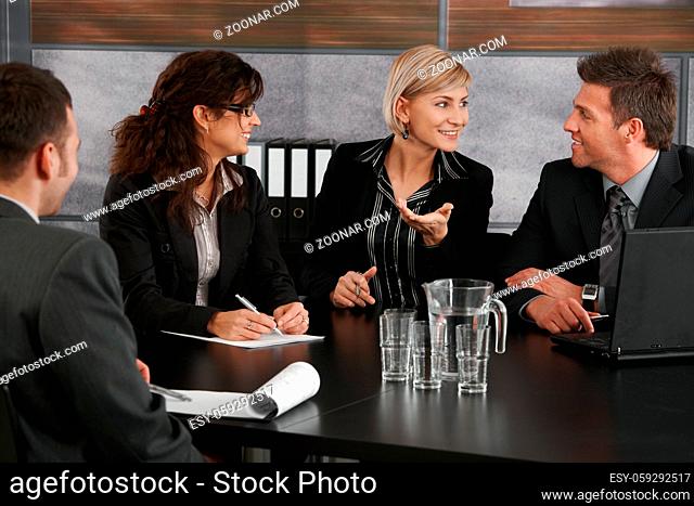 Young businesswoman explaining business problem, sitting at meeting table in office, others looking at her