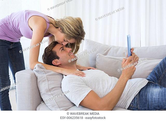 Moman kissing mans forehead while he using digital tablet