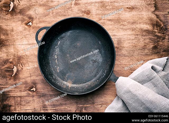 empty round black cast-iron frying pan with a handle on a brown wooden background, top view