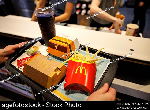 02 December 2021, Bavaria, Munich: A customer carries a tray with French fries, a Coca Cola, ketchup and a Big Mac in a branch of the fast food chain McDonald's...