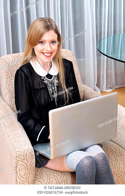 Young girl seating in armchair with laptop on her lap