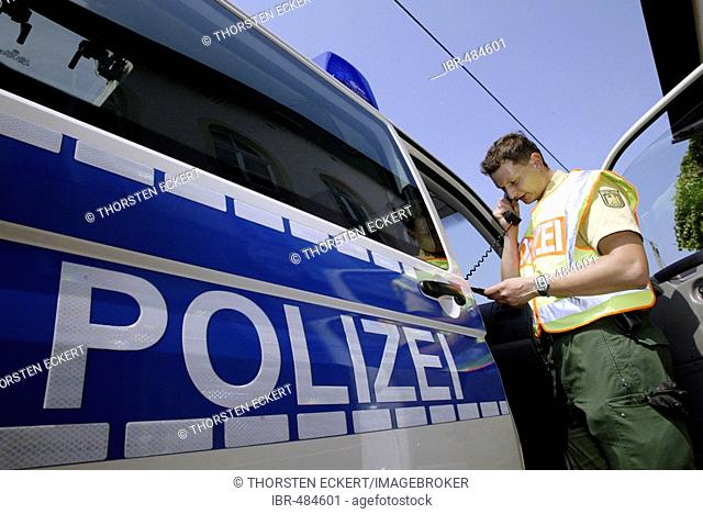A german police officer standing beside his car talking in a radiophone, near the czechian boarder, Saxony, Germany