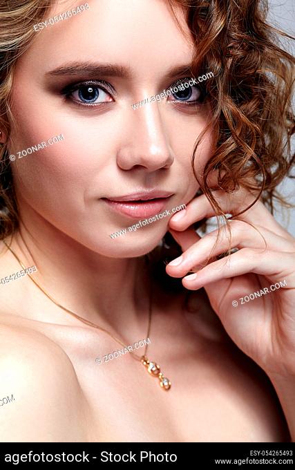Beauty portrait of young woman with hands near face. Female with curly hair on gray background