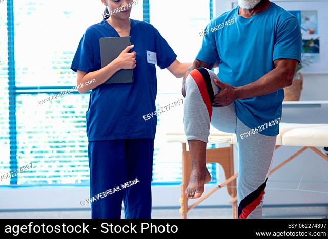 Diverse female physiotherapist and senior male patient holding leg in therapy, copy space
