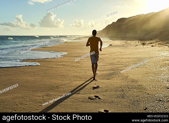 Man jogging on sand at beach during sunset