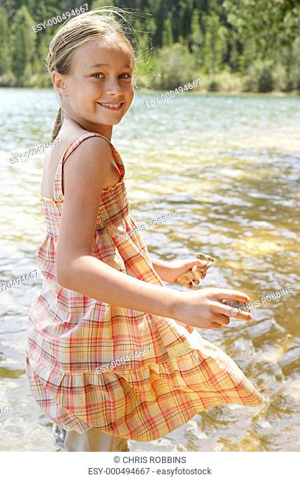 Girl 7-9 standing by lake holding stones portrait