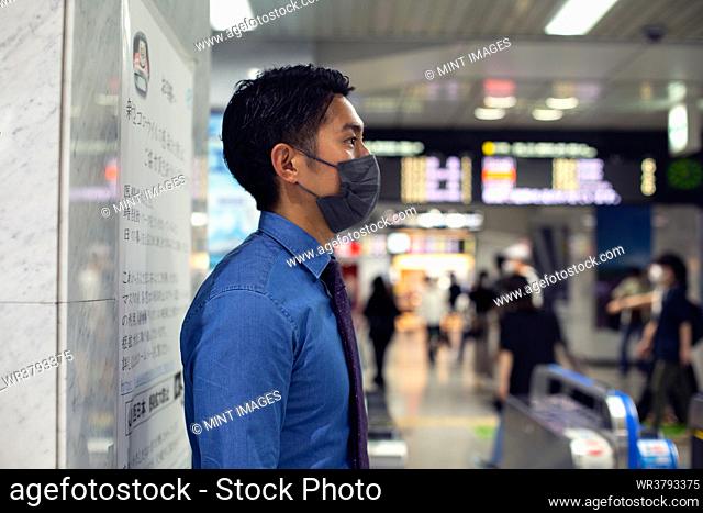 A young businessman in the city, on the move, standing at a metro station, wearing a face mask