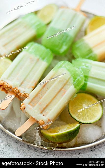 Summer refreshing homemade lime popsicles placed on metal tray with chipped ice over stone background, top view. Flat lay