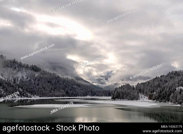 The Sylvensteinspeichersee at the edge of the Karwendel mountains in the Bavarian Alps in winter with snow and partly with ice, as well as cloud atmosphere