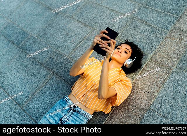Woman with headphones using smart phone lying on footpath
