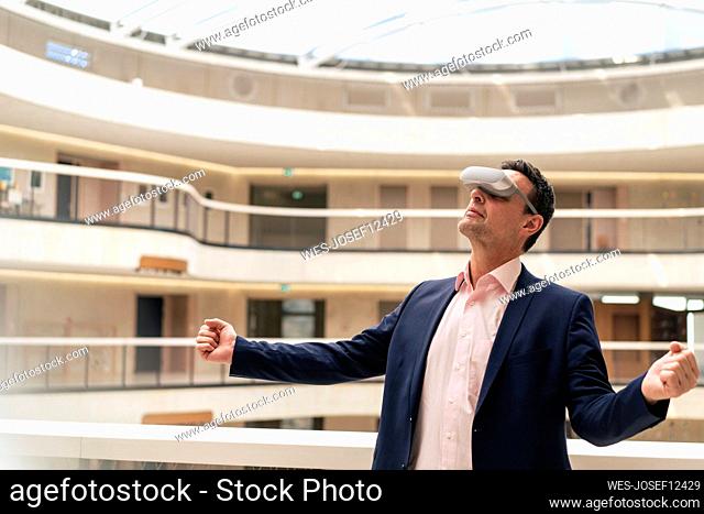 Mature businessman with VR glasses clenching fists in corridor