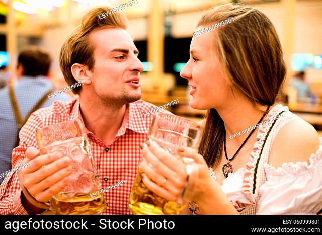 Young couple in traditional Bavarian Tracht - Dirndl and Lederhosen - in a beer tent at the Oktoberfest enjoying their beers and flirting with each other
