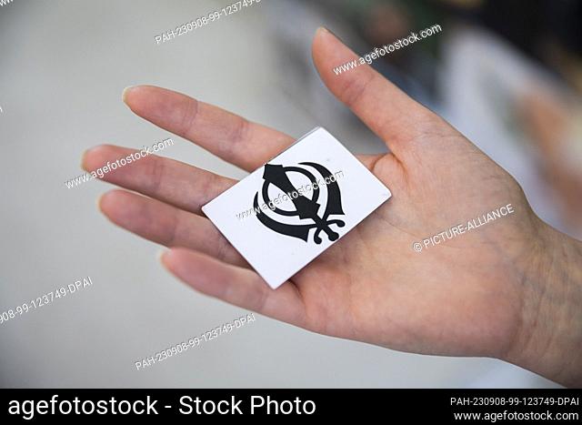 27 August 2023, Berlin: A woman holds the card of a memory game with the khanda, the religious symbol of Sikhism, at the 6th Berlin Festival of Religions