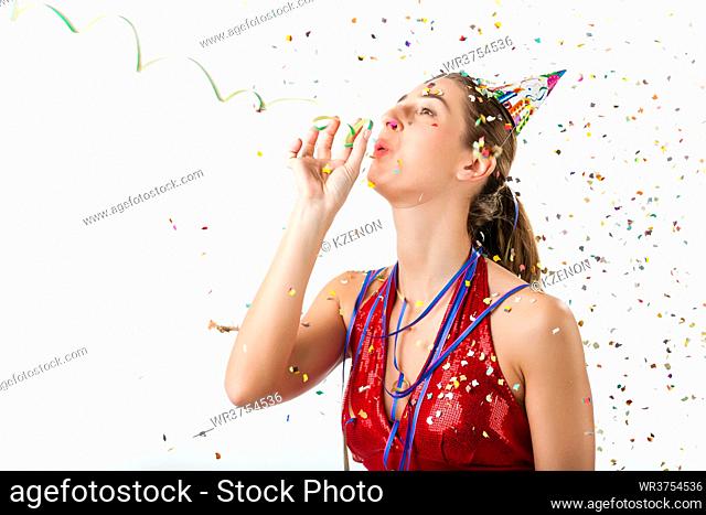 Woman celebrating birthday or new years eve and hooting with horn at a shower of confetti
