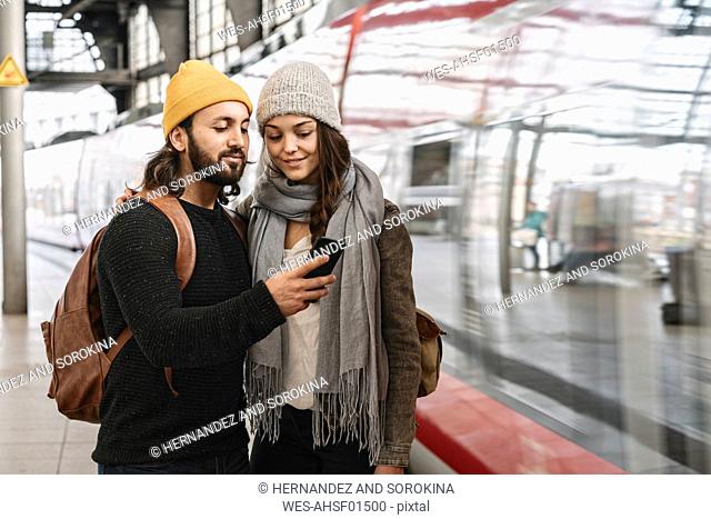 Young couple using smartphone at the station platform as the train comes in, Berlin, Germany