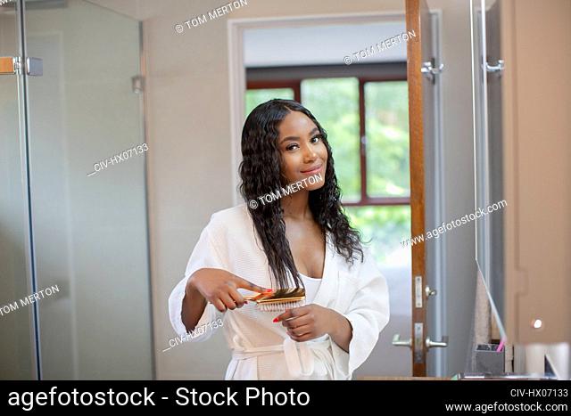 Portrait beautiful smiling young woman brushing hair in bathroom