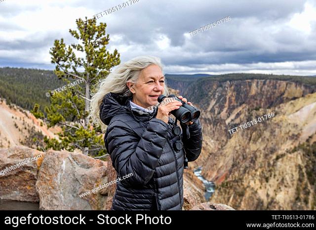 USA, Wyoming, Yellowstone National Park, Senior woman holding binoculars while standing above Grand Canyon in Yellowstone National Park