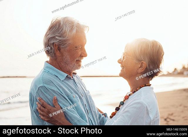 Close up of two cute and happy seniors having fun and enjoying together a sunset day at the beach. Mature couple in love looking each others