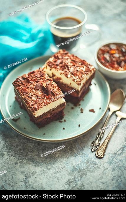 Delicious chocolate cake with layers served on ceramic blue plate. With cup of fresh black coffee. Placec on stone background table