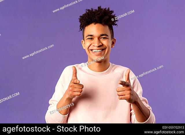 You got it. Close-up portrait of smiling cute young hispanic man saying good luck, pointing fingers at camera with pleased cute grin
