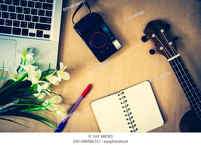 Top view of a laptop with a ukulele, cameras and notebooks on a flowers. Brown background Tone vintage