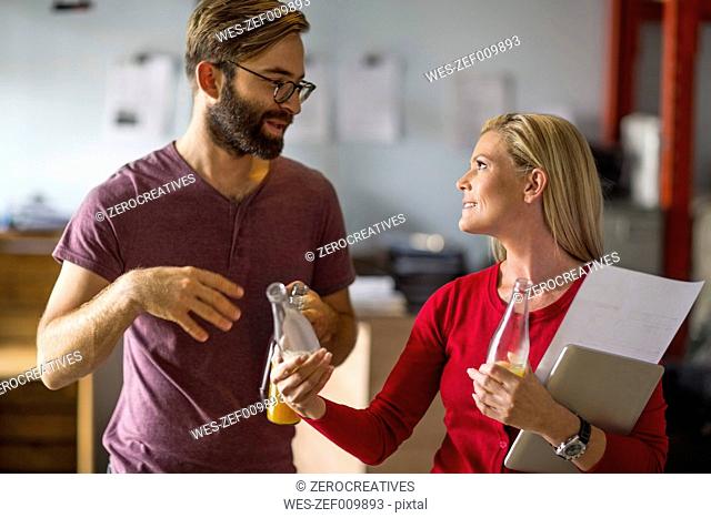 Man and woman discussing in warehouse holding juice bottles