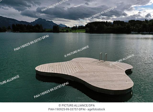 01 January 1970, Bavaria: Under dense clouds a deserted bathing platform floats on the Forggensee (aerial photograph with a drone)