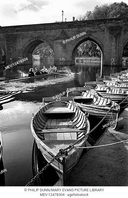 Rowers race past the traditional wooden hire boats tied up on the banks of the River Wear at Durham. They are about to go under the Elvet Bridge