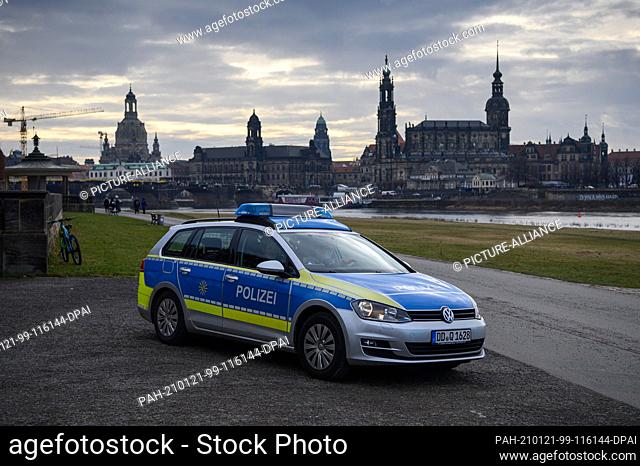 21 January 2021, Saxony, Dresden: A police car with policemen drives along the Elbe cycle path in front of the Old Town with the Frauenkirche (l-r)