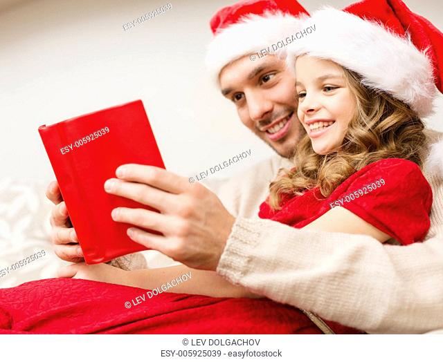 family, christmas, x-mas, winter, happiness and people concept - smiling father and daughter in santa helper hats reading book