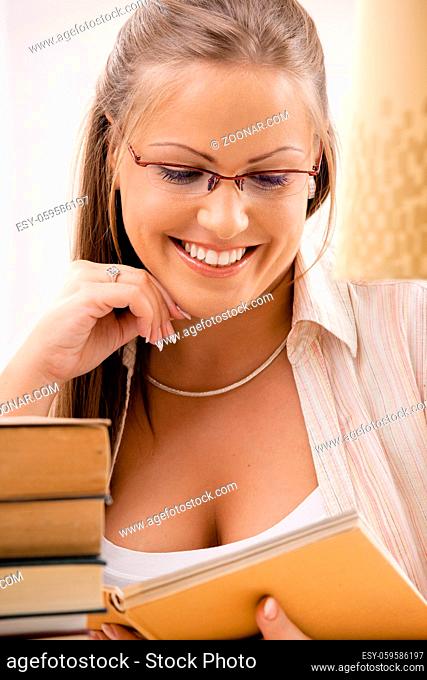 Happy student girl sitting at desk with pile of books, reading