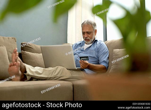 A SENIOR ADULT MAN USING DEBIT CARD AND LAPTOP FOR ONLINE PAYMENT