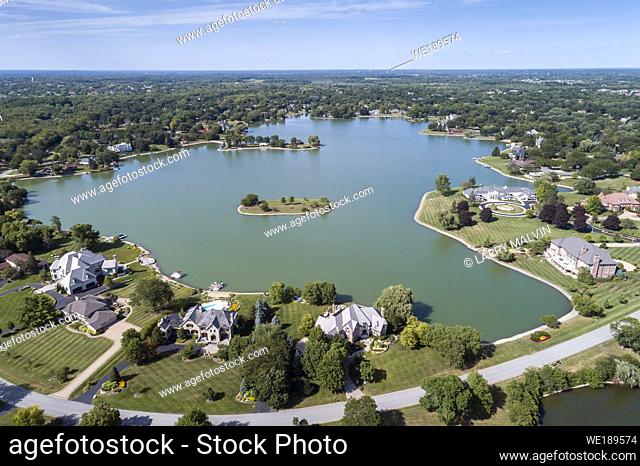 Aerial view of a tree-lined, upscale suburban neighborhood with a large lake in summer