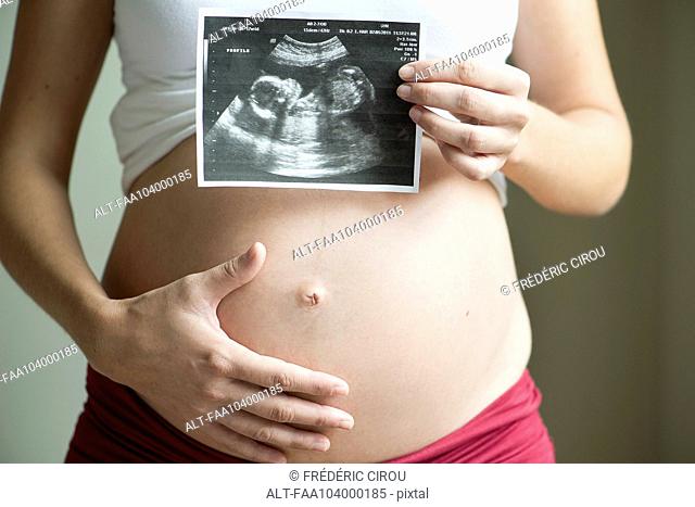 Pregnant woman holding ultrasound image, mid section