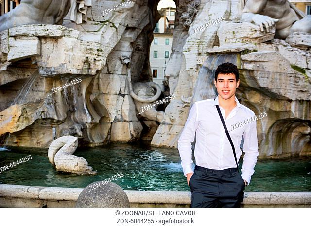 Smiling handsome young man posing in front of fountain in Navona Square, Rome, Italy