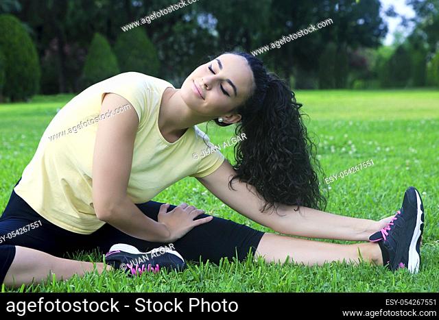 Portrait of beautiful black-haired sportswoman stretching on grass with eyes closed