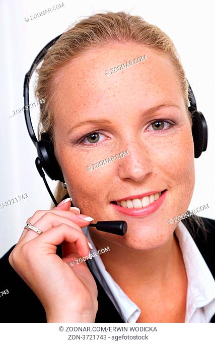Eine freundliche junge Frau mit Headset im Kundendienst telefoniert mit einem Kunden. Freundliche Hotline Mitarbeiterin