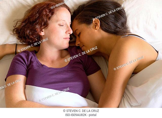 High angle view of lesbian couple lying in bed hugging, sleeping